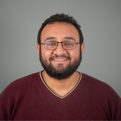 Omar Alsarayreh, smiling for a portfolio image. Short hair, wearing glasses, and with a burgunday shirt.